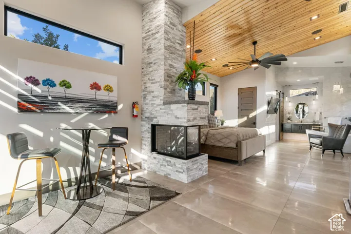 Vaulted wood-paneled ceiling, floor-to-ceiling stone fireplace, transom windows, ceramic tile flooring, and a ceiling fan