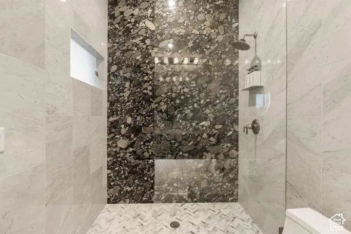 Shower featuring a patterned stone accent wall, light-toned tile walls, a built-in shower niche, a glass shower panel, and a mosaic tile floor