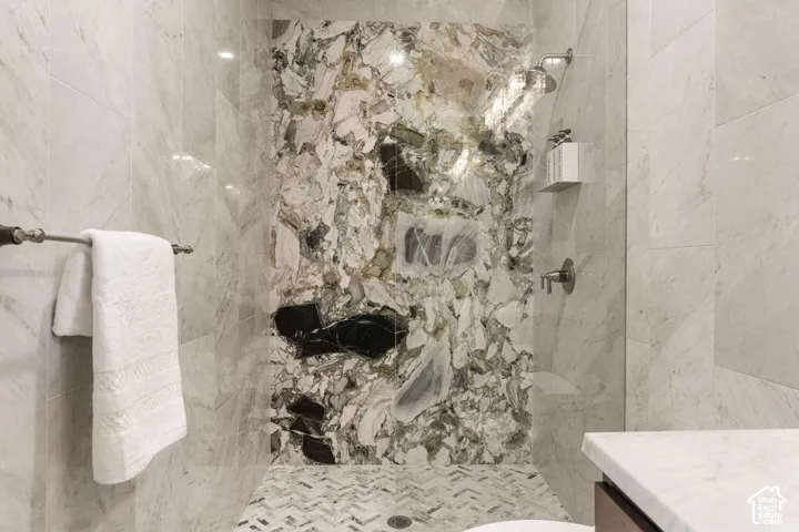 Shower with a distinctive natural stone accent wall, large format tile walls, and a mosaic tile floor in a chevron pattern
