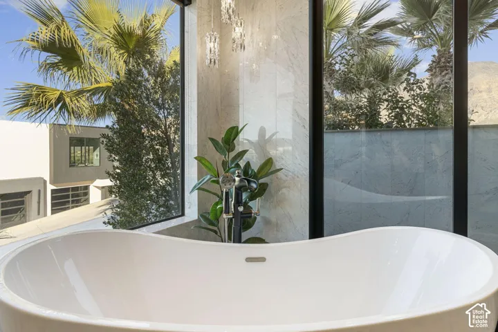 Freestanding soaking tub with a modern floor-mounted faucet, large format tile wall, and expansive window with black framing