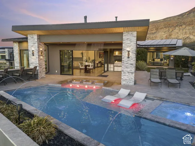 Outdoor living space with a swimming pool, integrated spa, and an outdoor kitchen featuring a built-in grill