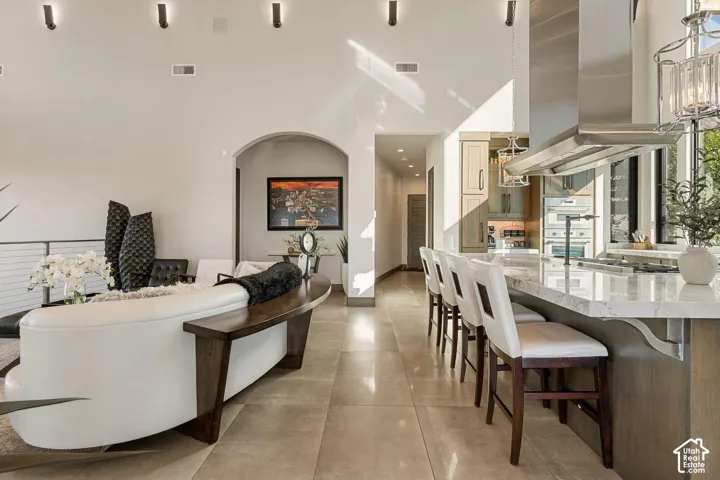 Open concept living space featuring a spacious kitchen island with seating, stainless steel range hood, and tile flooring