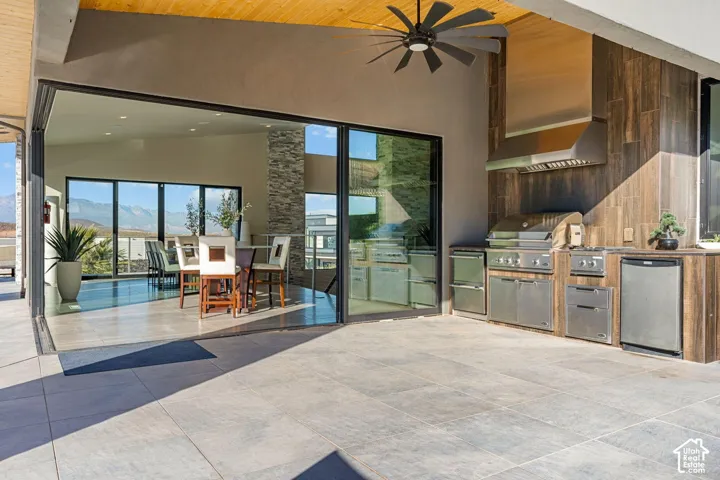 Expansive outdoor living area featuring a built-in kitchen with stainless steel appliances, a wood-finish ceiling with a ceiling fan, and large format tile flooring