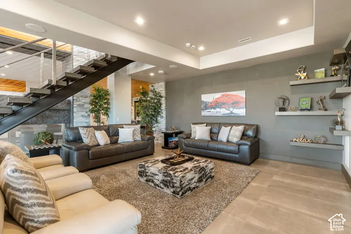 Open-concept living space showcasing light wood-finish flooring, a coffered ceiling with recessed lighting, and gray accent wall paneling