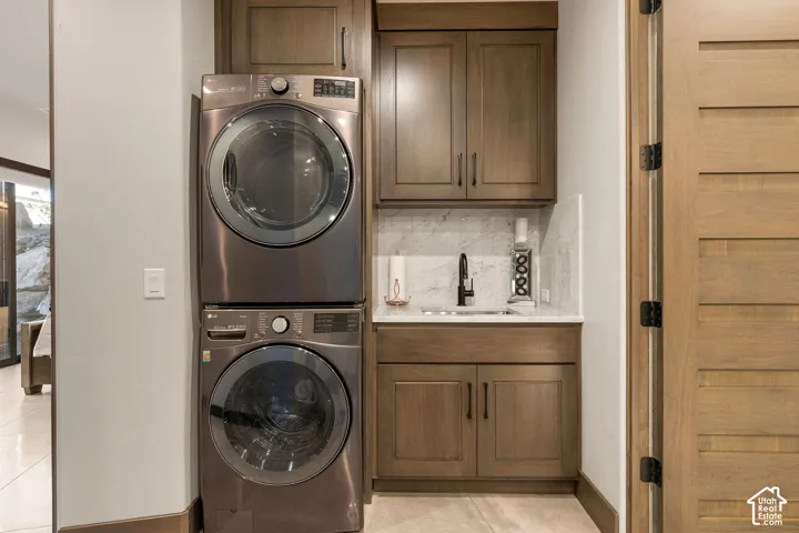 Stacked washer and dryer, wood-finish cabinetry, white countertop, marble-look backsplash, and a black gooseneck faucet