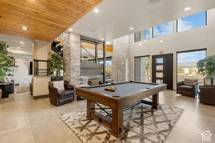 Vaulted ceilings with clerestory windows, wood-paneled ceiling accent, stone accent columns, large format tile flooring, and a contemporary entry door with frosted glass inserts