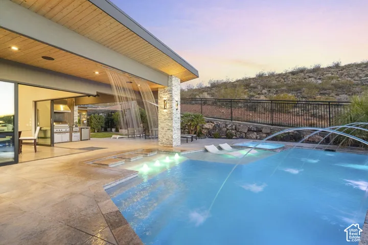 Swimming pool with integrated water features, adjacent spa, and expansive patio