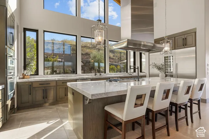High ceilings with clerestory windows, stainless steel appliances, a large island with countertop seating, wood-finish cabinetry, and tiled flooring