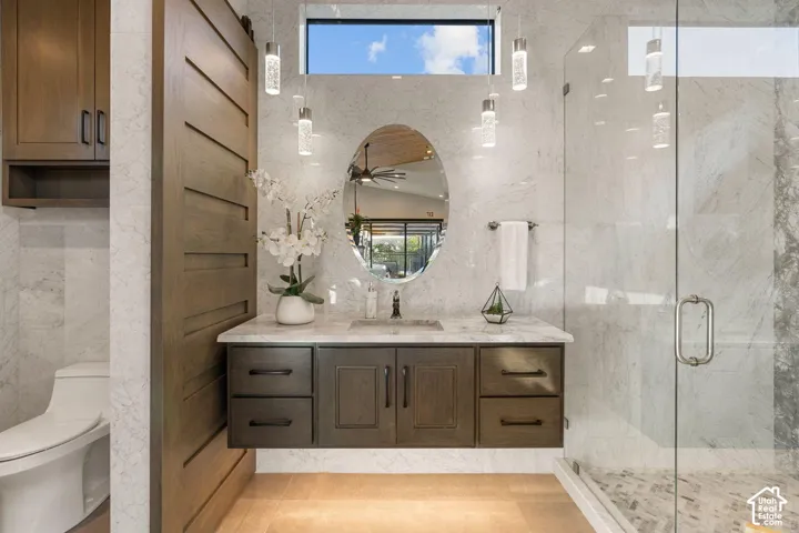 Floating vanity with an oval mirror, clear glass enclosed shower, full-height wall tiling, and wood-finish flooring