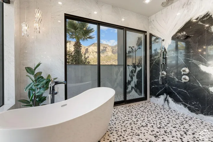 Freestanding soaking tub, floor-to-ceiling black-framed sliding glass doors, dual shower system with polished chrome fixtures, black and white marble shower surround, and mosaic pebble floor
