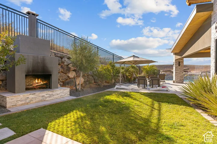 Landscaped backyard featuring a built-in outdoor fireplace with stone accents, a manicured lawn, and a paved patio area