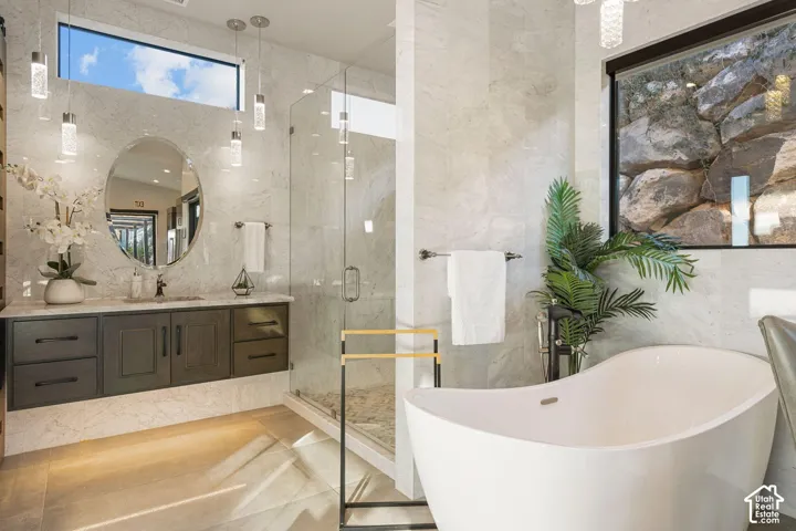 Floating vanity with a stone countertop and an oval mirror, glass-enclosed shower, freestanding soaking tub, and pendant lighting