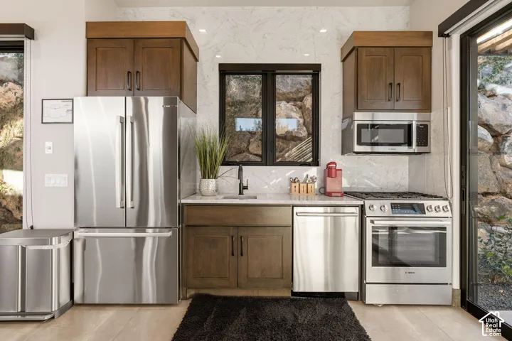 Kitchen featuring stainless steel appliances, dark wood cabinetry, white stone countertops, and a full-height tile backsplash
