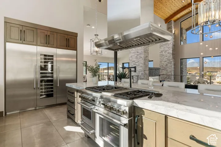 Gourmet kitchen with professional-grade stainless steel appliances, large center island with cooktop, built-in wine refrigerator, and high vaulted ceilings with wood-paneled accents