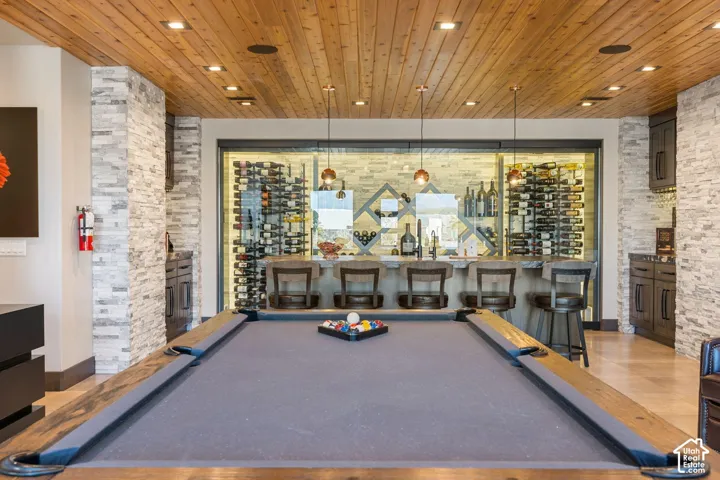 Recreation room featuring a pool table, wood-paneled ceiling, stone accent walls, a built-in bar, and a glass-enclosed wine storage area