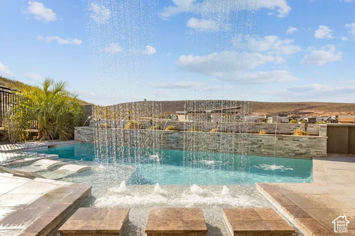 Integrated pool with water features, shallow lounging area, and stone-clad retaining wall