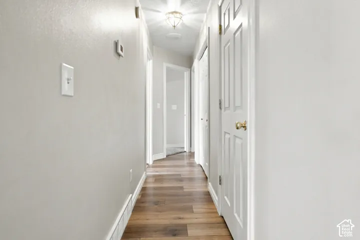 Hallway featuring wood-finish flooring, light-toned walls, and white paneled doors with brass hardware