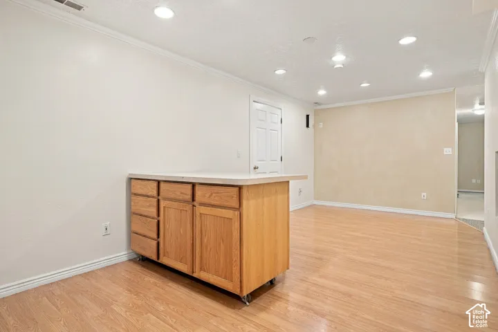 Wood-finish flooring with a light wood mobile cabinetry island, light-toned countertop, recessed lighting, and crown molding