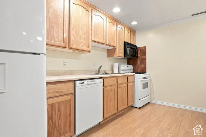 Kitchen featuring wood-finish cabinetry, light-toned countertops, a stainless steel sink, and wood-finish flooring