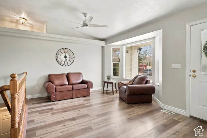 Wood-finish flooring, bay window, vaulted ceiling, ceiling fan, and decorative railing