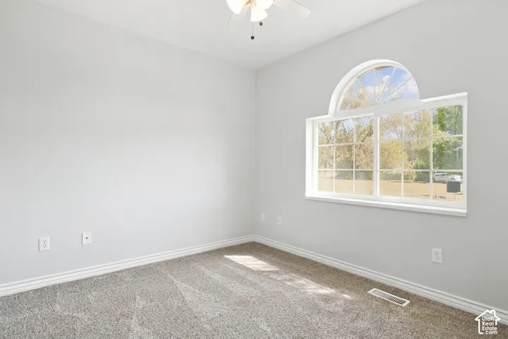 Arched window with gridded panes, ceiling fan, neutral wall tones, and plush carpet flooring