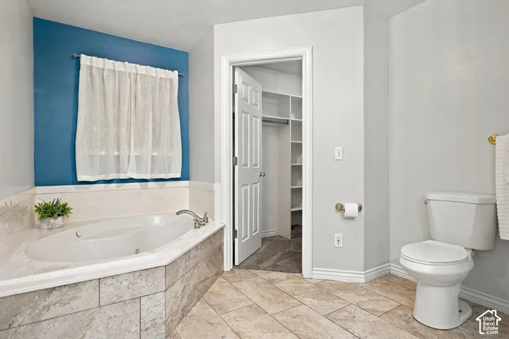 Corner soaking tub with tiled surround, adjacent commode, and a built-in closet with shelving