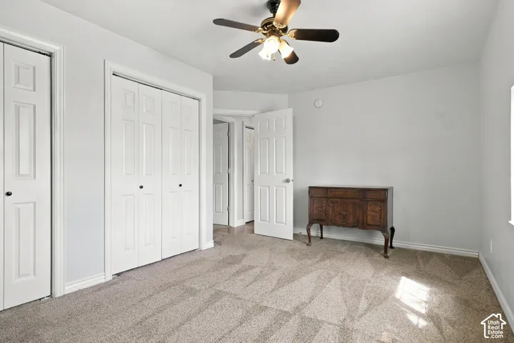 Carpeted room featuring multiple panel doors, a ceiling fan with integrated lighting, and a window for natural light