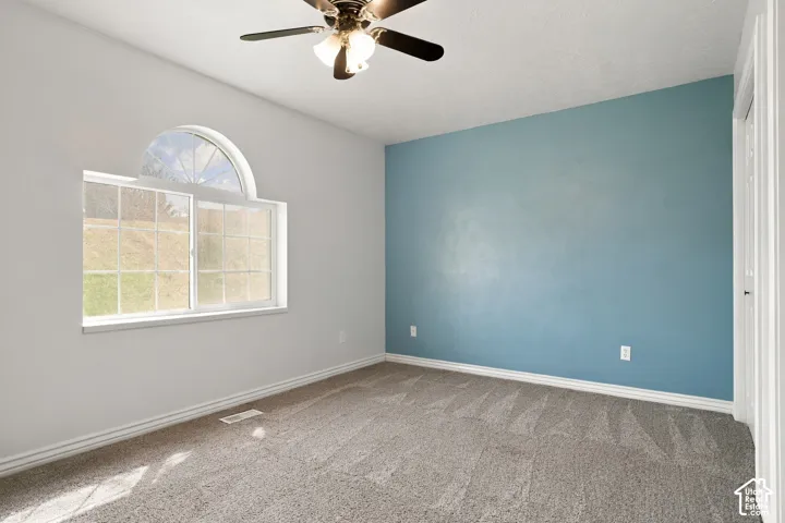 Arched transom window above a multi-pane window, ceiling fan with integrated lighting, and neutral carpet flooring