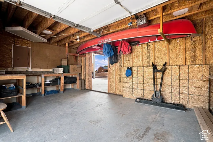 Attached garage with exposed wood framing, concrete flooring, and built-in workbench