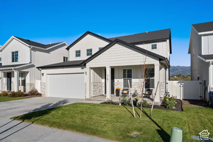 Modern farmhouse exterior with white vertical siding, a covered front porch, an attached garage, a manicured lawn, and a mountain backdrop