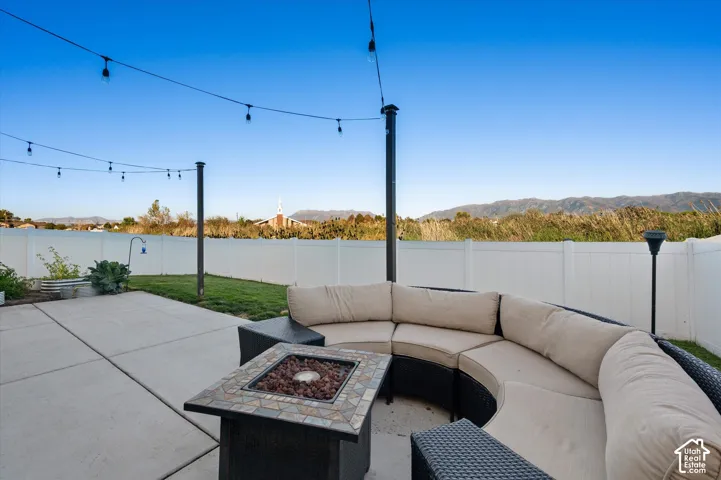 Paved patio with a built-in fire pit, string lighting, and a white privacy fence