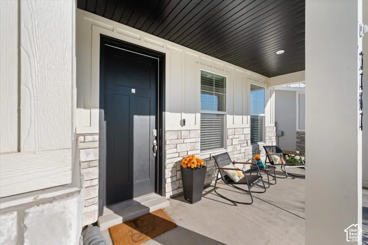 Covered front porch featuring a dark entry door, stone and board-and-batten facade, and recessed lighting