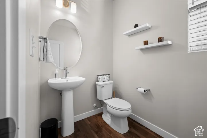 Pedestal sink with a polished chrome faucet, oval mirror, wall-mounted light fixture, wood-finish flooring, and two floating wall shelves
