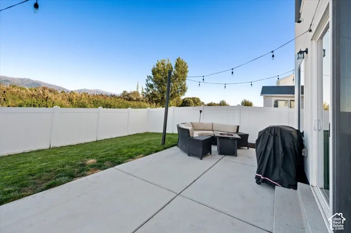 Concrete patio with string lighting, a white privacy fence, and a grass area