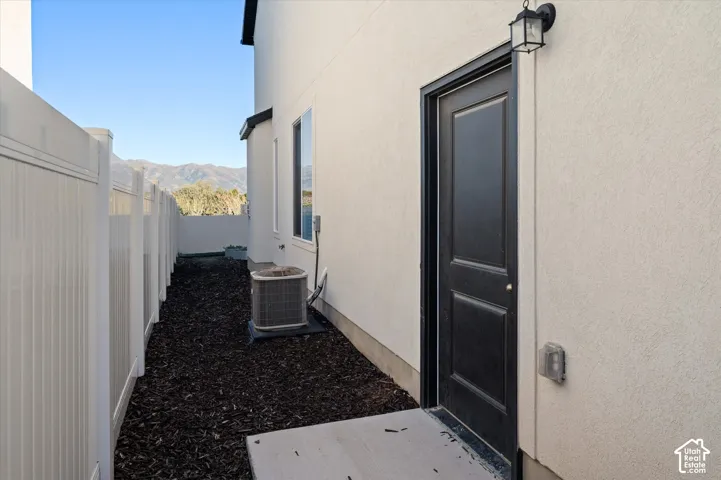 White privacy fencing enclosing a narrow exterior area with dark mulch, a black exterior door, an outdoor wall sconce, and a window