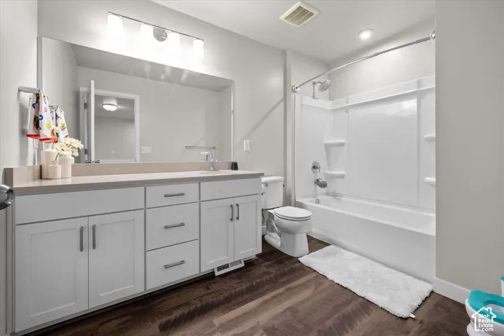 Spacious bathroom featuring a white vanity with extensive storage, a large mirror, a combined shower and tub, and wood-finish flooring