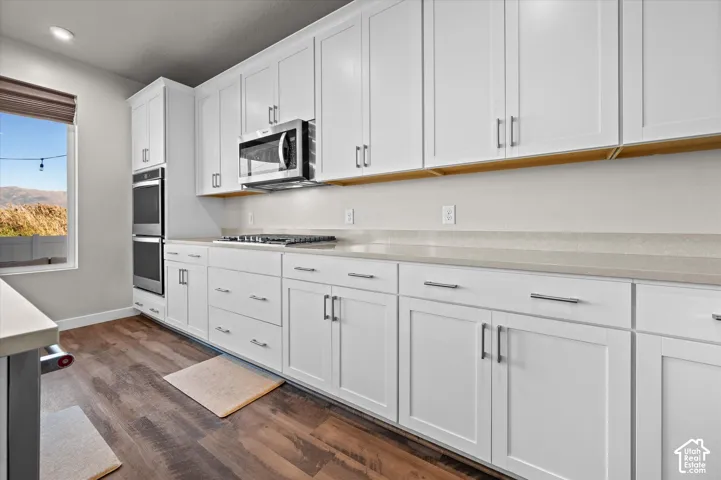White shaker cabinetry, stainless steel double oven, microwave, gas range, and wood-finish flooring