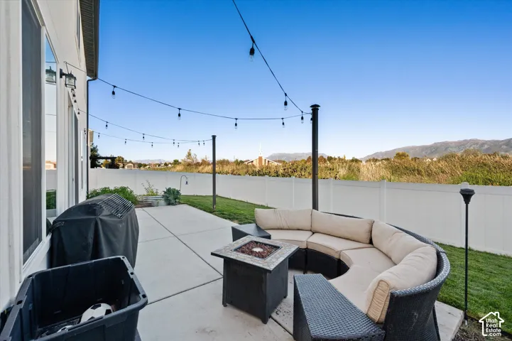 Expansive concrete patio with string lighting, surrounded by a white privacy fence and green lawn