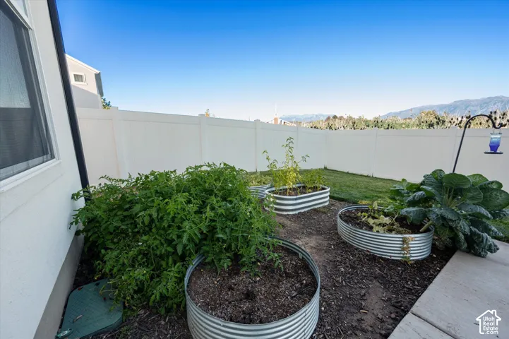 Backyard featuring a white privacy fence, three corrugated metal raised garden beds, a concrete patio section, and a manicured lawn area