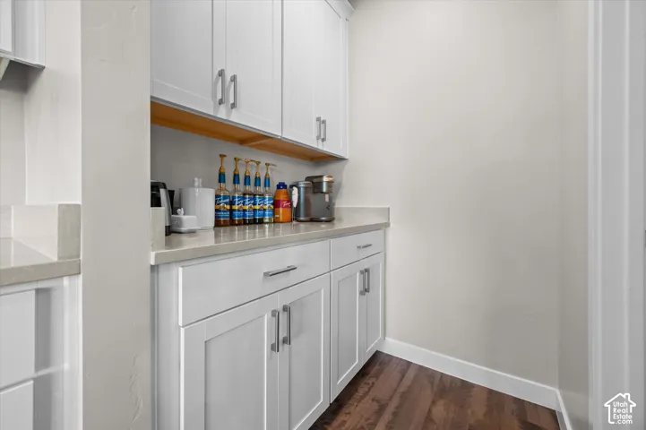 White shaker-style cabinetry with chrome pulls, light-toned countertop, wood-finish flooring, and open shelving butler pantry/coffee bar