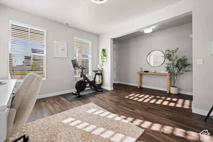 Spacious room featuring wood-finish flooring, two large windows with blinds, and light gray walls