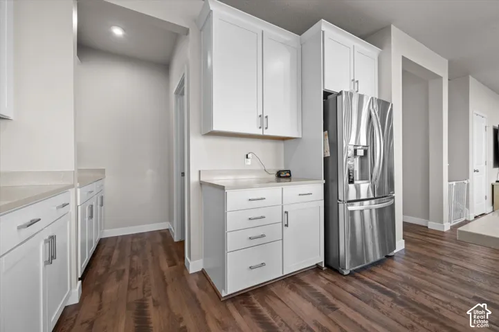 White shaker cabinetry with brushed nickel hardware, light-toned countertops, stainless steel refrigerator, and wood-finish flooring