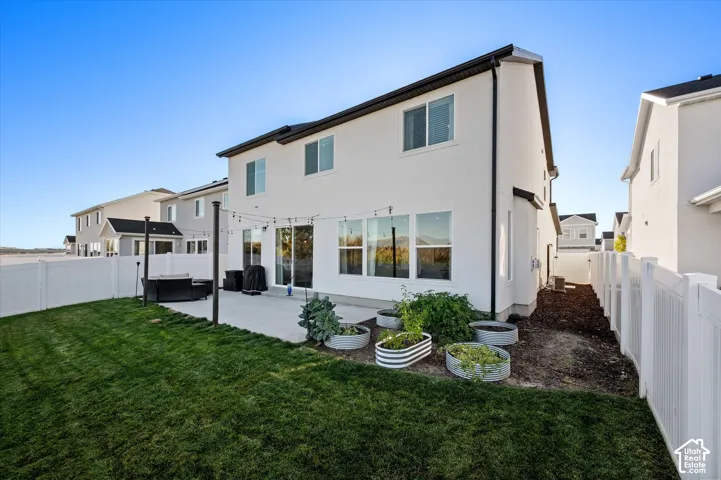 Expansive rear yard featuring a manicured lawn, concrete patio, and white vinyl fencing