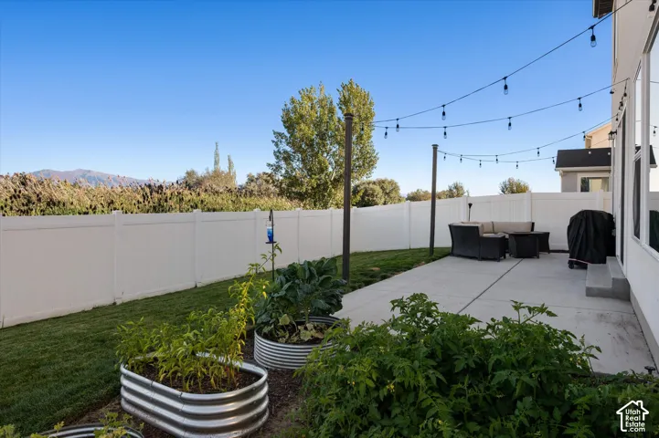 Expansive concrete patio with string lighting, surrounded by a white privacy fence