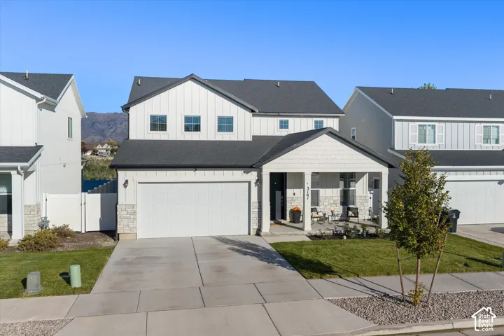 White siding exterior with a dark shingle roof, attached two-car garage, covered porch entry, and a concrete driveway
