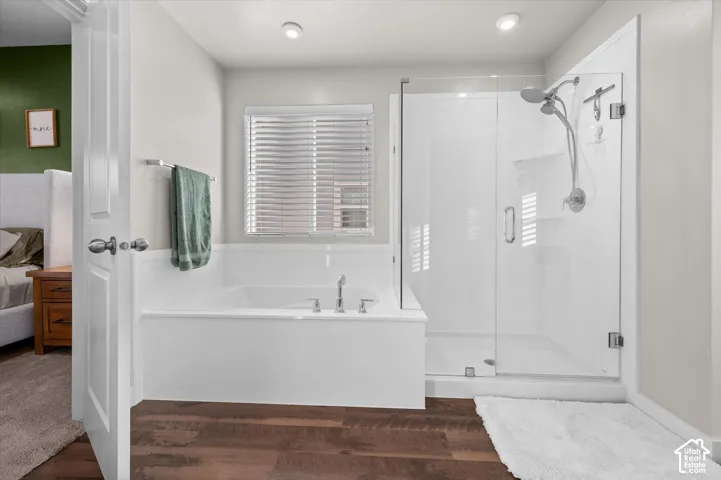 Bathroom featuring a built-in soaking tub, separate glass-enclosed shower, wood-finish flooring, and recessed lighting