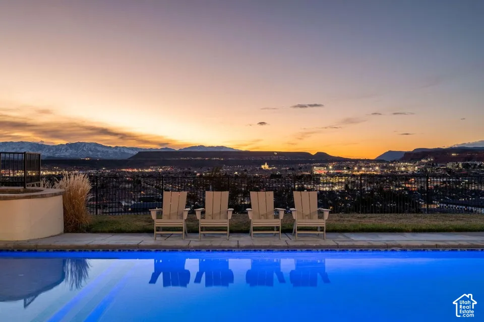Infinity-edge pool with blue tile border, surrounding paved patio, and mountain backdrop