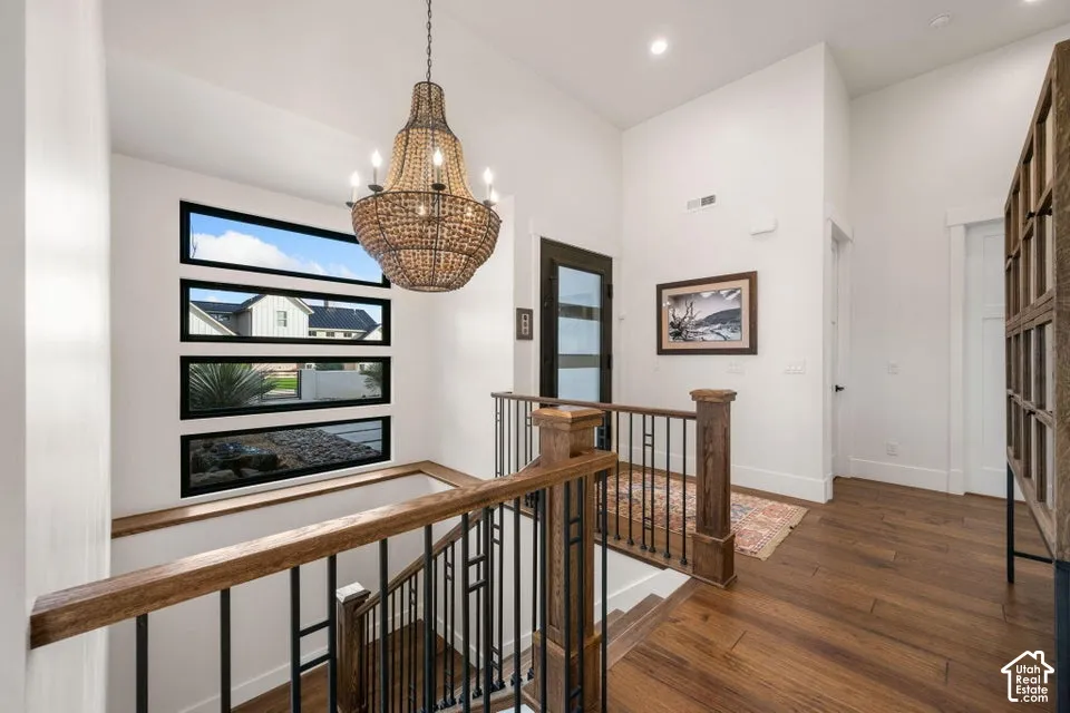 Vaulted ceiling with a beaded chandelier, wood-finish flooring, custom wood and wrought iron staircase, black-framed horizontal windows, and a black-framed glass-paneled door