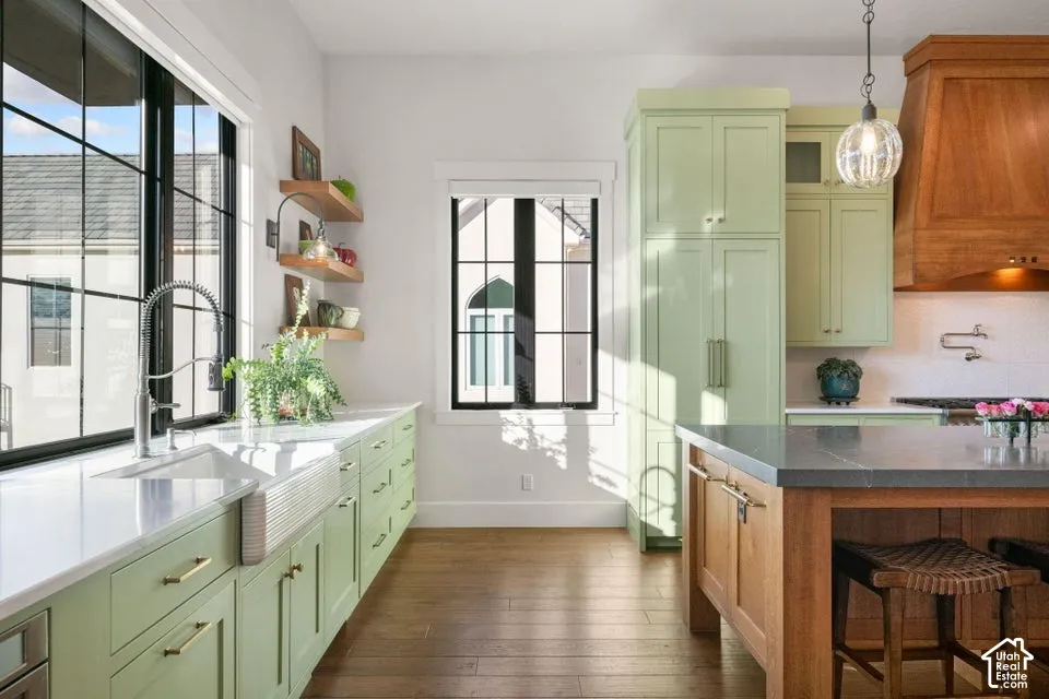 Kitchen featuring wood-finish flooring, light green cabinetry, a large kitchen island with a stone countertop, a farmhouse sink, and black-framed windows