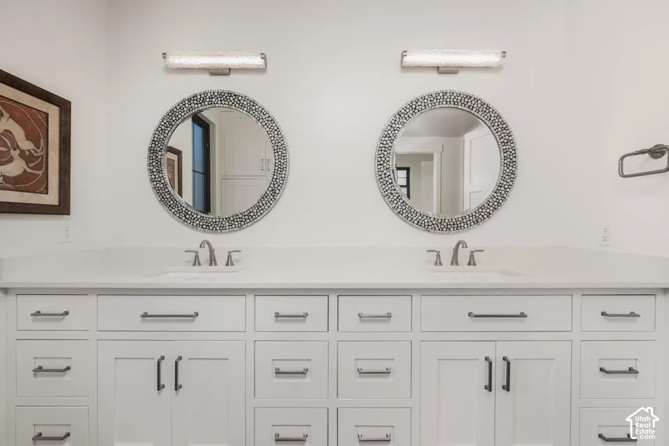 Dual vanity with white cabinetry, integrated sinks, brushed nickel fixtures, and decorative round mirrors